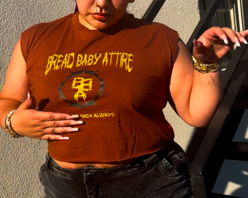 wearing a brown t-shirt with yellow text and graphics, standing against a gray wall.